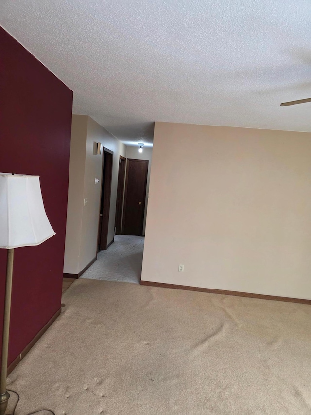 empty room with light carpet, baseboards, and a textured ceiling