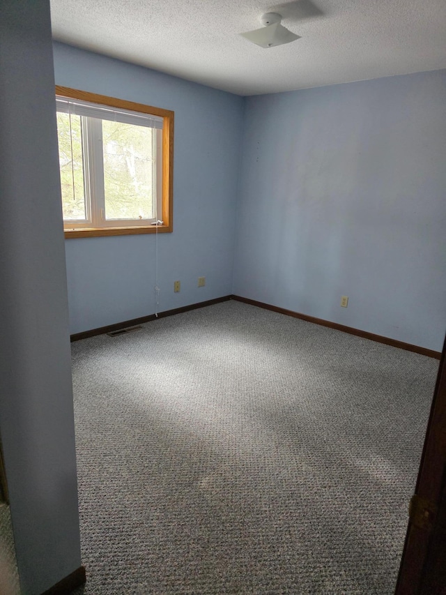 carpeted spare room featuring baseboards, a textured ceiling, and visible vents