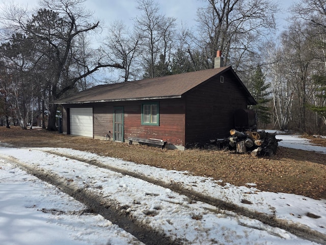 snow covered property featuring an attached garage and a chimney