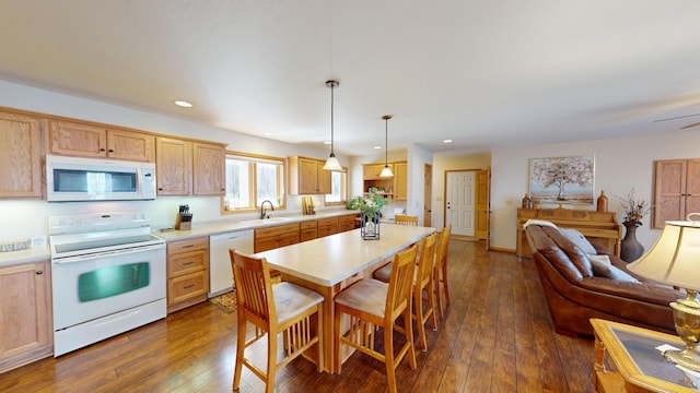 kitchen featuring a breakfast bar, a sink, white appliances, light countertops, and open floor plan