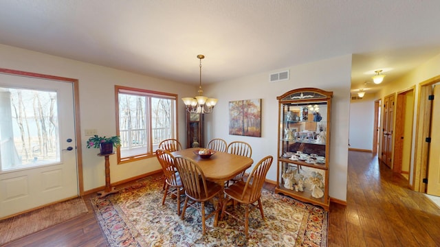 dining space with baseboards, visible vents, an inviting chandelier, and hardwood / wood-style flooring