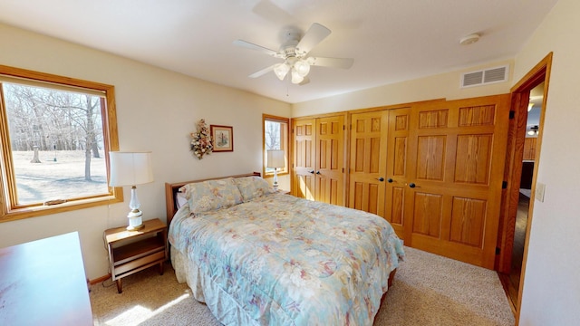 carpeted bedroom featuring ceiling fan, visible vents, and multiple windows