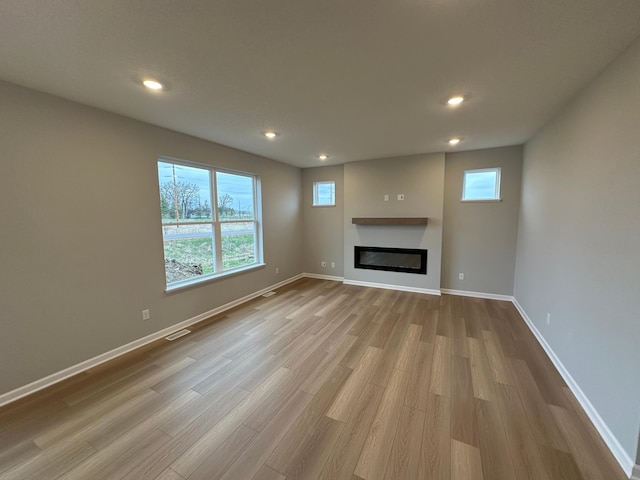 unfurnished living room with wood finished floors, visible vents, a glass covered fireplace, and recessed lighting