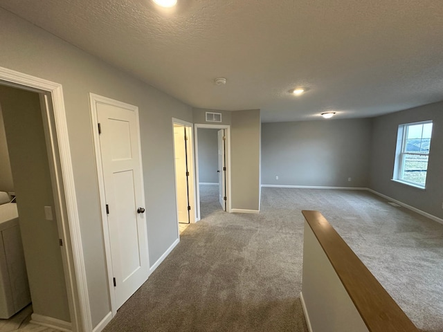 corridor with a textured ceiling, visible vents, carpet floors, and baseboards