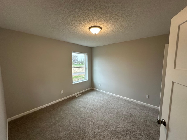 empty room with a textured ceiling, visible vents, dark carpet, and baseboards