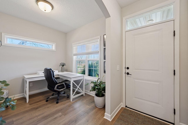 office area featuring arched walkways, a textured ceiling, baseboards, and light wood-style floors