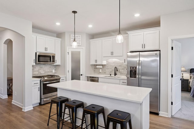 kitchen with wood finished floors, light countertops, white cabinetry, a sink, and appliances with stainless steel finishes