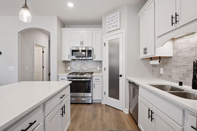 kitchen with white cabinets, appliances with stainless steel finishes, a sink, arched walkways, and backsplash