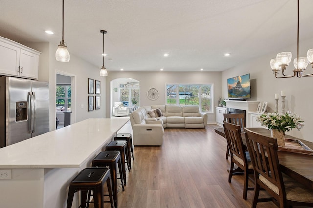 kitchen with stainless steel fridge with ice dispenser, light countertops, arched walkways, wood finished floors, and a kitchen island