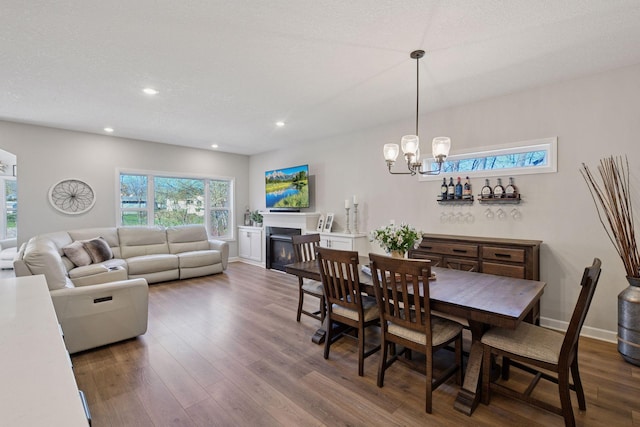 dining space with recessed lighting, dark wood finished floors, a glass covered fireplace, and an inviting chandelier