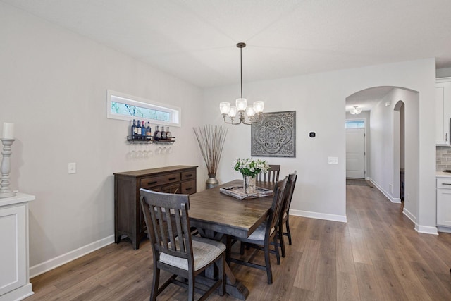 dining space featuring baseboards, arched walkways, dark wood finished floors, and an inviting chandelier