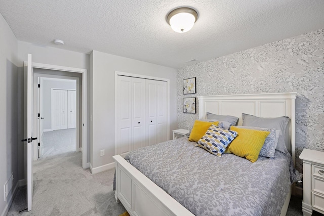 bedroom featuring a closet, light carpet, baseboards, wallpapered walls, and a textured ceiling