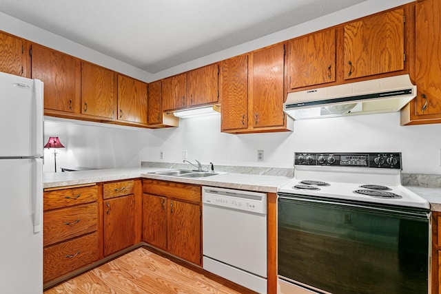 kitchen with light countertops, under cabinet range hood, a sink, and white appliances