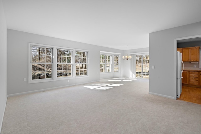 unfurnished living room with an inviting chandelier, baseboards, and light carpet