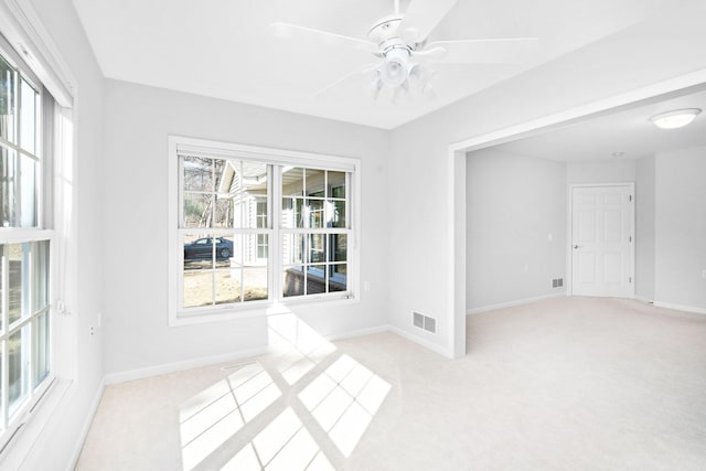 spare room with light colored carpet, baseboards, ceiling fan, and visible vents