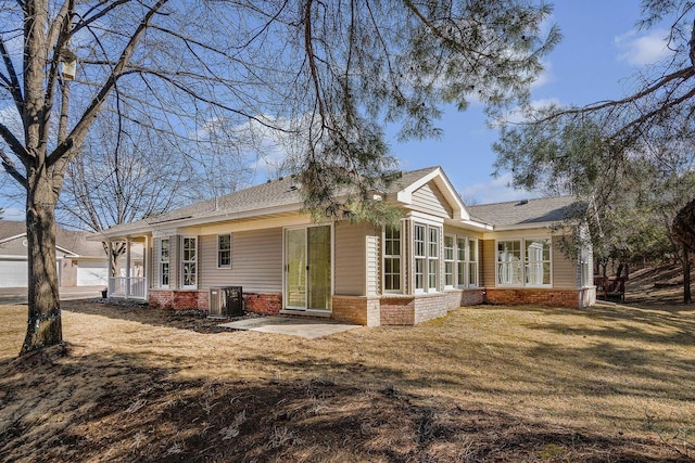 back of house with central air condition unit, a shingled roof, a lawn, and brick siding