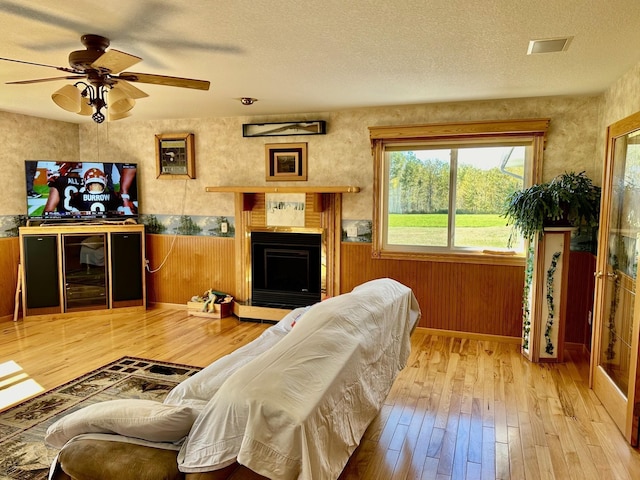 16335 County Road 2, Brainerd, MN 56401 - living area featuring hardwood / wood-style floors, a wainscoted wall, a fireplace with raised hearth, a ceiling fan, and a textured ceiling