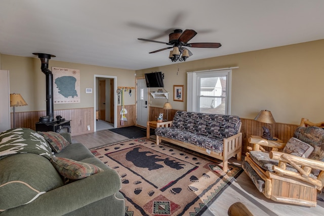 5591 Wildwood Ave, Isle, MN 56342 - living room featuring a wainscoted wall, a wood stove, ceiling fan, wood finished floors, and wooden walls