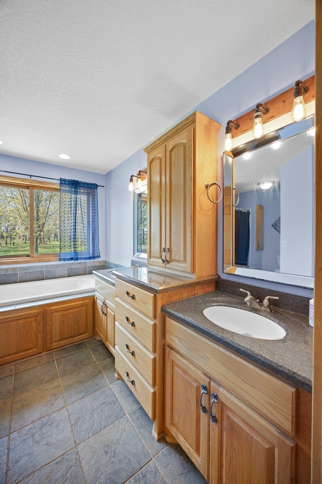 bathroom featuring stone tile floors, vanity, a bath, and a textured ceiling