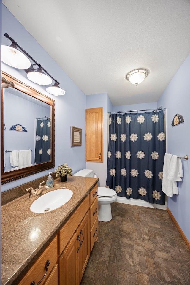 full bathroom featuring baseboards, stone finish flooring, vanity, toilet, and curtained shower