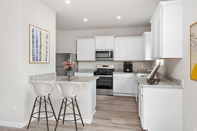kitchen featuring a peninsula, white cabinetry, a breakfast bar, a sink, and stainless steel appliances