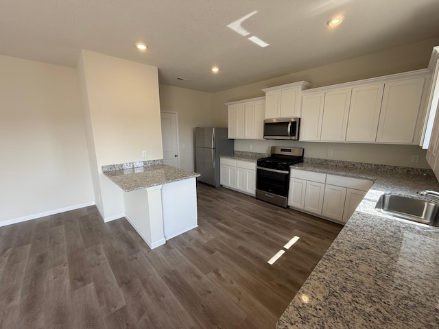 kitchen with a sink, appliances with stainless steel finishes, a peninsula, dark wood-style floors, and white cabinetry