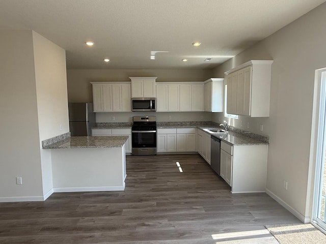 kitchen with appliances with stainless steel finishes, wood finished floors, a sink, and white cabinetry