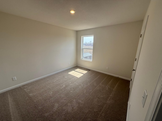 spare room featuring dark colored carpet and baseboards