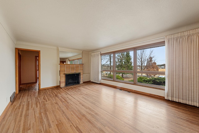 unfurnished living room with light wood finished floors, a fireplace, a textured ceiling, baseboards, and visible vents