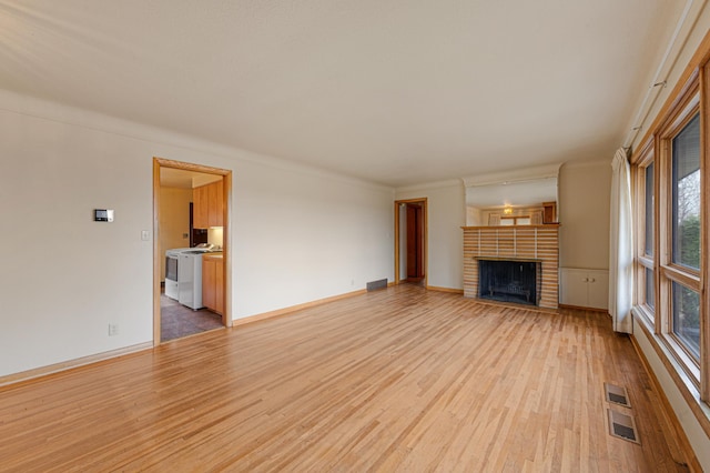 unfurnished living room with visible vents, baseboards, a fireplace, light wood-style floors, and washer / dryer