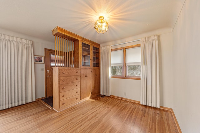 unfurnished bedroom with baseboards, light wood-type flooring, and an inviting chandelier
