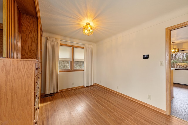 spare room with hardwood / wood-style floors, baseboards, visible vents, and an inviting chandelier