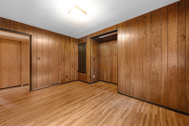 spare room featuring baseboards, visible vents, wooden walls, and wood finished floors