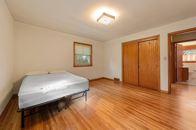 bedroom with a closet, baseboards, light wood-style floors, and visible vents