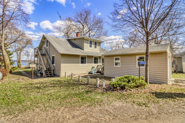 back of house featuring a deck, a chimney, a shingled roof, a lawn, and stairway