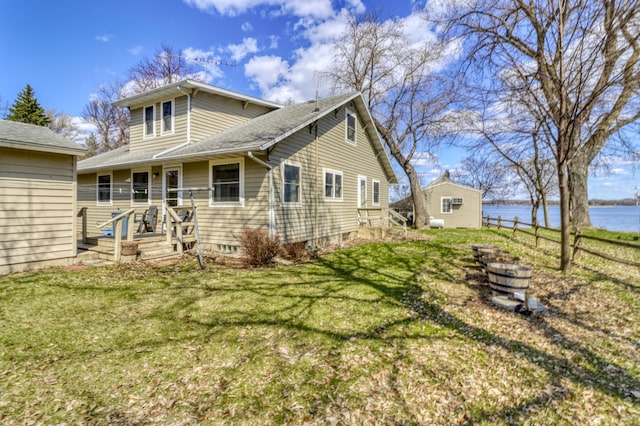 back of property with a yard, a water view, fence, and a shingled roof