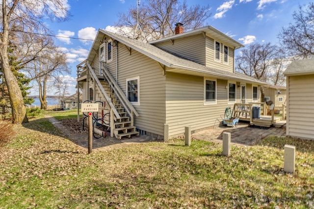 rear view of house featuring roof with shingles, stairs, a deck, a chimney, and a yard