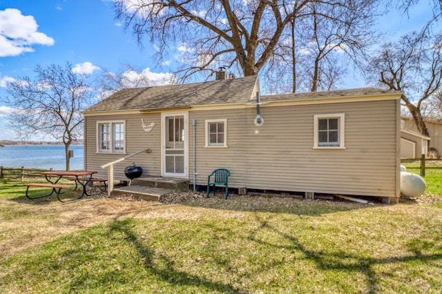 back of property featuring a shingled roof, a chimney, a yard, and a water view
