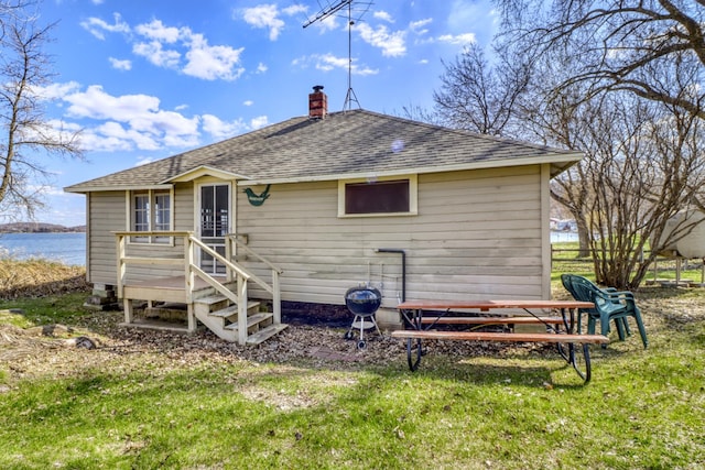 rear view of house with roof with shingles, a chimney, a yard, and a water view