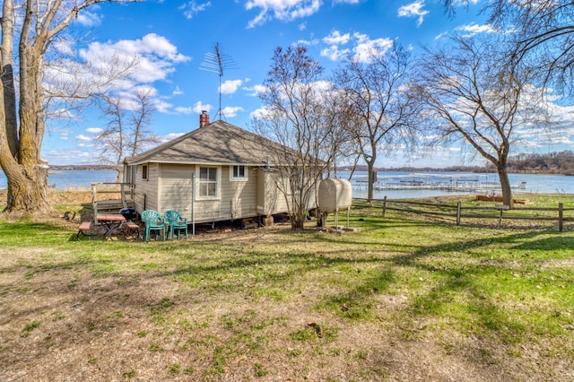 view of side of property with a lawn, fence, a water view, and a chimney
