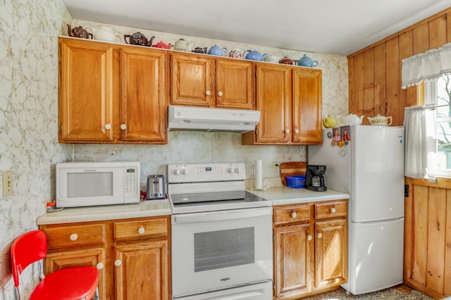 kitchen featuring white appliances, wallpapered walls, under cabinet range hood, and light countertops