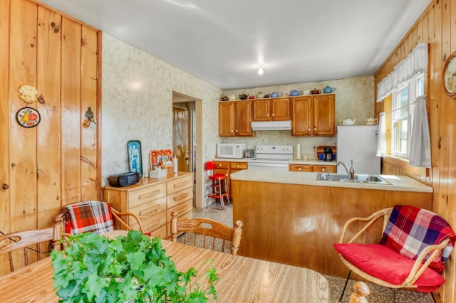 kitchen featuring a sink, light countertops, a peninsula, under cabinet range hood, and white appliances
