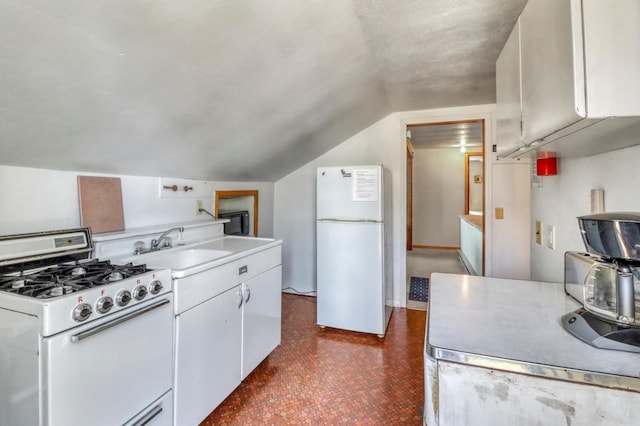 kitchen with white appliances, light countertops, white cabinets, a sink, and vaulted ceiling