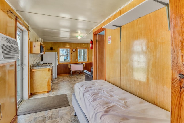 bedroom featuring a sink, a wall unit AC, wooden walls, and freestanding refrigerator