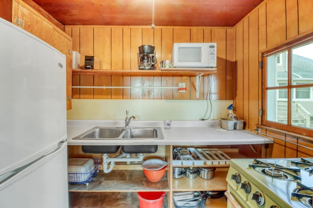 kitchen featuring white appliances, wooden walls, light countertops, wood ceiling, and a sink