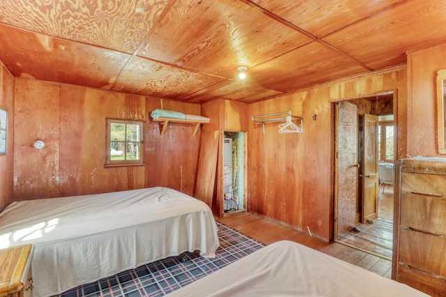 bedroom with wooden walls, wood ceiling, water heater, and hardwood / wood-style floors