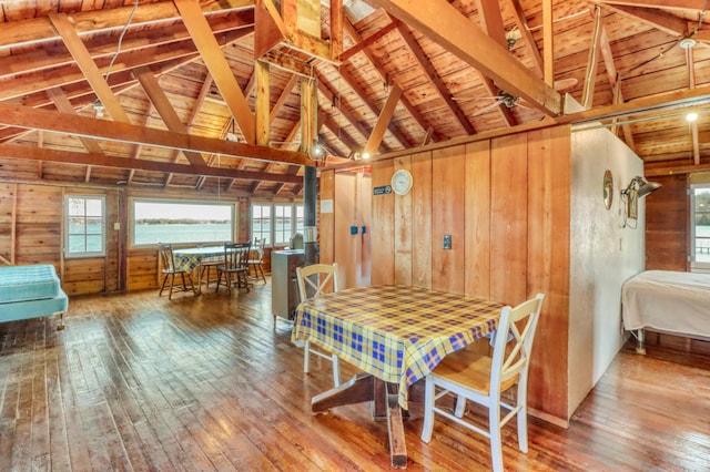 dining space with vaulted ceiling with beams, wood walls, and hardwood / wood-style floors