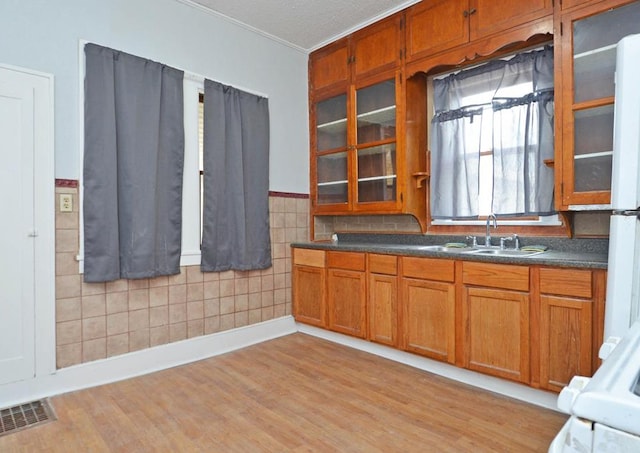 665 Bedford St, Saint Paul, MN 55130 - kitchen featuring light wood finished floors, brown cabinets, crown molding, dark countertops, and glass insert cabinets