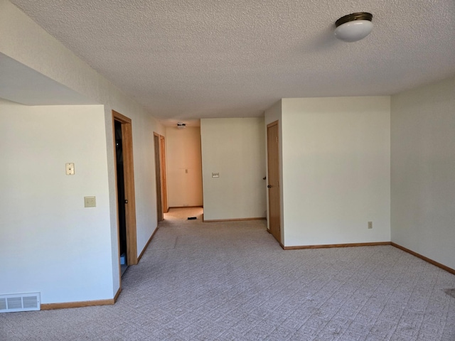 spare room with visible vents, a textured ceiling, and light colored carpet