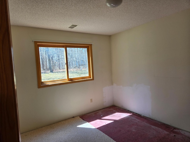 carpeted spare room featuring a textured ceiling and visible vents
